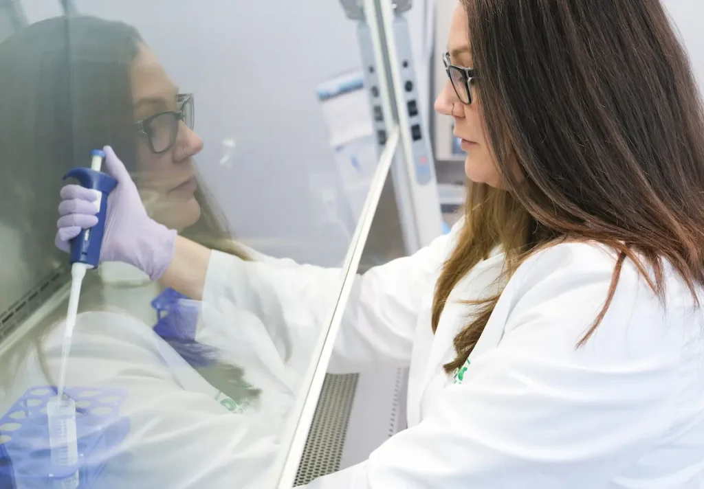 Scientist in a lab coat using a pipette under a protective laboratory hood.